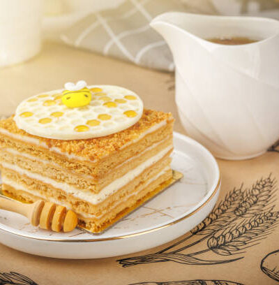 Napoleon cake with cup of honey on tablecloth, closeup