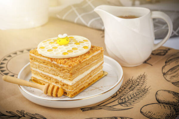 Napoleon cake with cup of honey on tablecloth, closeup
